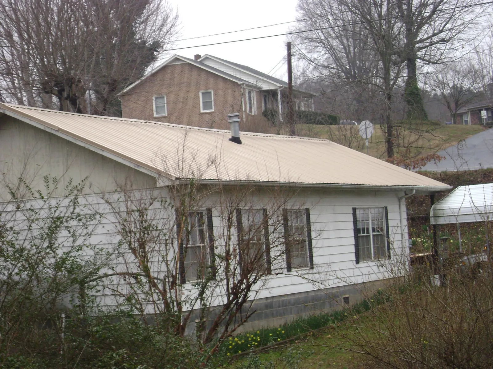 Tan metal roof on a white sided house set into a hillside — Commercial Roofing by Roofing Brothers in Buchanan